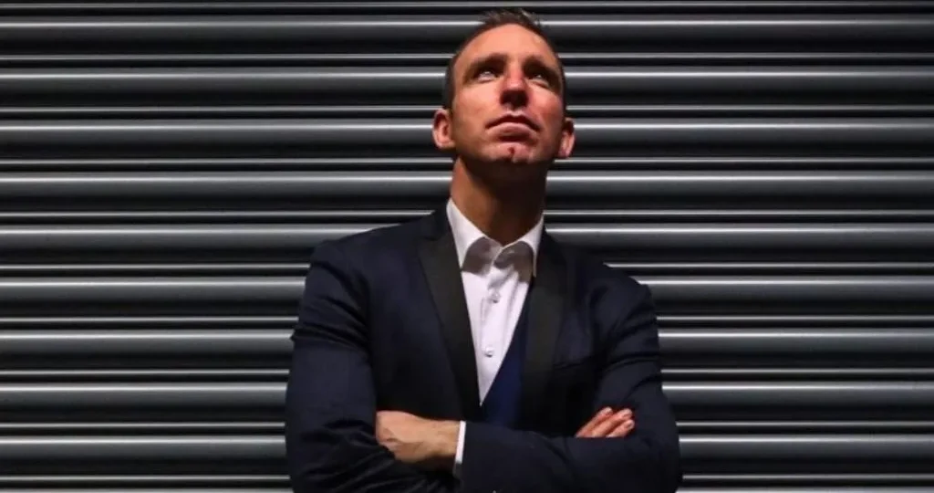Author Enda McNulty standing with arms crossed in front of a metal shutter, looking upwards.