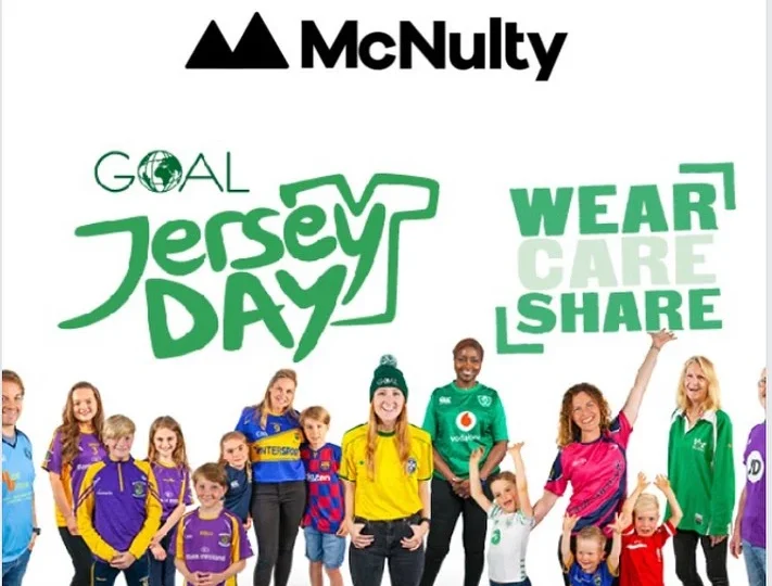 Group of people of various ages wearing different sports jerseys, standing and smiling in front of a banner with the text "Goal Jersey Day" and "Wear Care Share."