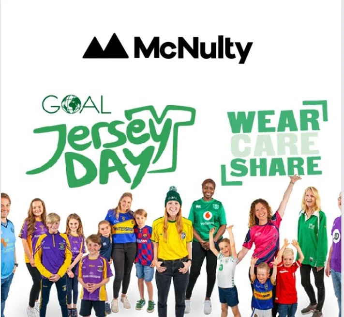 Group of people of various ages wearing different sports jerseys, standing and smiling in front of a banner with the text "Goal Jersey Day" and "Wear Care Share."