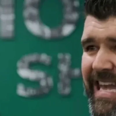 Nick Winkelman speaking energetically with a green background and partial text visible behind him.