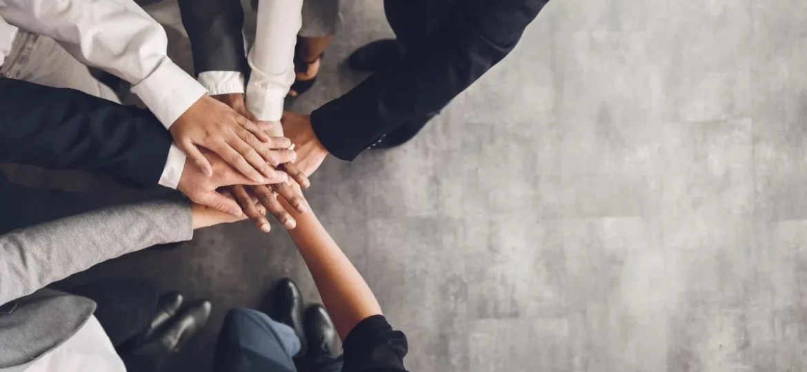 A diverse group of professionals joining hands in a unified team effort, symbolising high performance and collaboration.